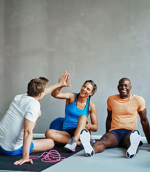 Three adults relax after a workout, sharing a high-five and smiles during a supportive fitness class community at Krav Maga Chapel Hill.