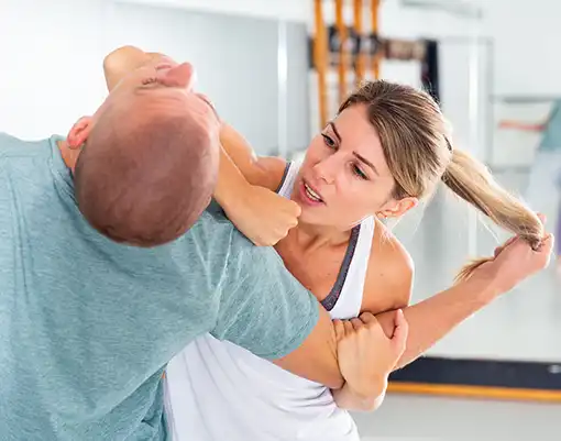 Woman demonstrates a Krav Maga self-defense technique by controlling an attacker’s arm during a realistic partner training session at Krav Maga Chapel Hill.